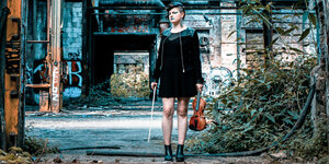 Die Jazz-Musikerin Zuzana Leharová steht mit ihrer Violine auf einem alten Gelände mit Graffiti