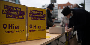 Ein Mann unterschreibt einen Unterschriftenliste neben zwei Plakaten auf einem Tapeziertisch. Auf den Plakaten steht: Deutsche Wohnen und Co. Enteignen - hier unterschreiben