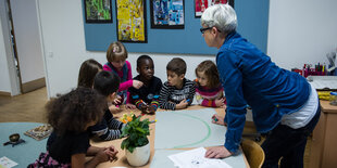 Eine Frau stützt sich auf einen Tisch, an dem Kinder sitzen