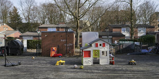 Asphaltfläche mit Spielzeug und einem Spielhaus, im Hintergrund Bäumde und einstöckige Ziegelhäuser