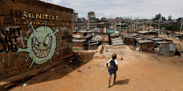 Ein Junge geht an einer Wand mit Graffiti vorbei auf ein Slum zu