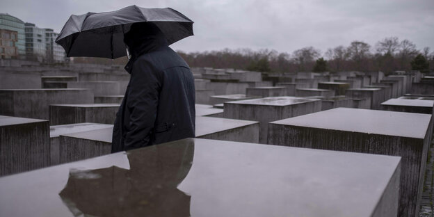ein Mann mit regenschirm läuft durch das Denkmal für die ermordeten Juden Europas in Berlin