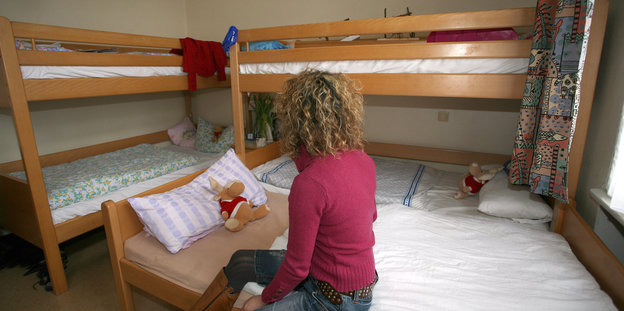 Frau auf einem Bett in einem Zimmer, dahinter zwei weitere Doppelstockbetten.