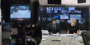 Studio des Fernsehsenders Doschd mit Kamera, Moderator und Moderatorin am Tisch - Monitore der Redaktion im Hintergrund