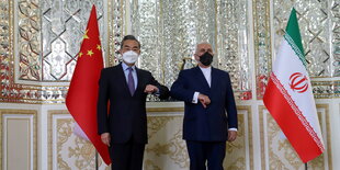 Chinas Außenminister Wang Yi und der iranische Außenminister Mohammed Dschawad Sarif machen einen Ellenbogencheck vor den jeweiligen Länderflaggen China/Iran