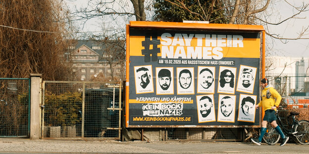 Ein Plakat zeigt die Köpfe der Opfer des rassistischen Anschlags von Hanau. Darunter stehen ihre Namen, darüber der Hashtag "Say Their Names". Neben dem Plakat läuft ein Jogger.