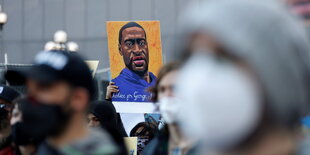 Demonstrantinnen halten ein Schild in die Höhe, das George Floyd gedenkt