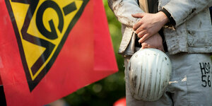 Stahlarbeiter beteiligen sich an einem Warnstreik - IGM Flagge und Mann in Arbeitskleidung der seinen Helm hält