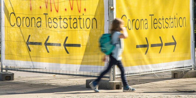 Kind vor Wegweisern zur Corona Impfstation