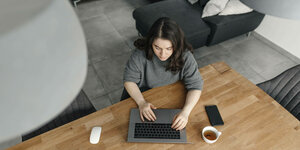 Eine Frau sitzt am Tisch und arbeitet am Laptop