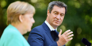 Markus Söder schaut während einer Pressekonferenz im Freien zu Angela Merkel