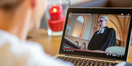 Ein Mann schaut sich einen Online Gottesdienst auf Youtube an - auf dem Laptopmonitor sieht man eine Pastorin