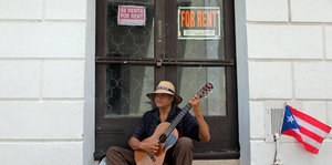Bettelnder Mann mit Gitarre vor verrammeltem Geschäft