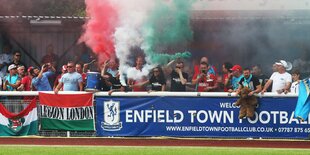 Fußballfans hinter einer Werbebande entzünden Bengalo-Feuer