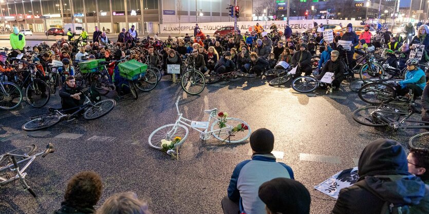 Menschen sitzen auf Straße um weißes "Geisterrad"