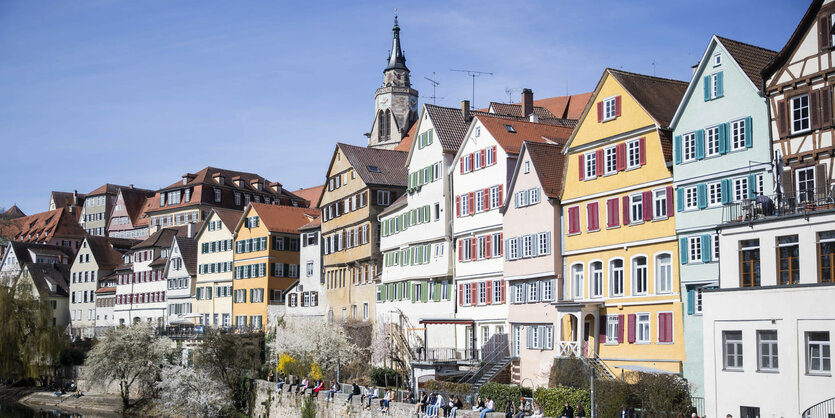 Menschen sitzen auf einer Mauer an einem Fluss vor Altstadthäusern