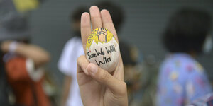Ein Demonstrant zeigt den Drei-Finger-Gruß als Zeichen des Widerstands und hält dabei ein Osterei mit der Aufschrift "Sure we will win" (Wir werden sicher gewinnen)
