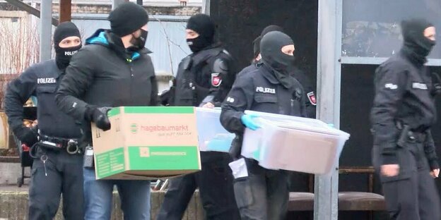 Polizisten tragen sichergestelltes Material während einer Razzia aus einem Gebäude.