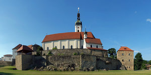 Hübsche Kirche mit mittelalterlicher Stadtmauer vor strahlend blauem Himmel