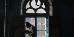 Ein Mann mit Kippa schaut in ein Gebetsbuch, dahinter ein verziertes Fenster