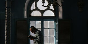 Ein Mann mit Kippa schaut in ein Gebetsbuch, dahinter ein verziertes Fenster