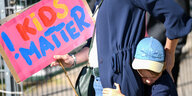 Ein Kind hält sich an seiner Mutter fest. Die hält ein Schild, auf dem "Kids Matter" in bunten Buchstaben steht.