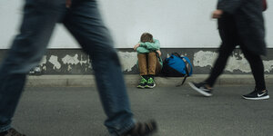 Ein Junge sitzt zusammengekauert am Straßenrand.