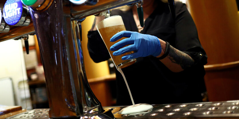 Eine Person hinter einem Pub-tresen zapft ein Bier und trägt blaue Gummihandschuhe