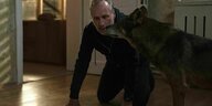 Filmszene: Mann kauert in einem Wohnraum, neben ihm ein Wolf