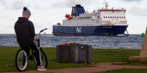 Ein Junge auf einem BMX Fahrrad beobachtet eine eine Fähre in der Näge des Hafens Larne in Nordirland