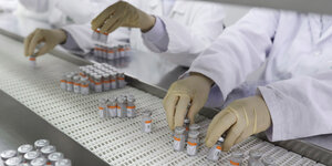 Zwei MitarbeiterInnen legen Ampullen mit Covid-19 Impfstoff auf ein Förderband