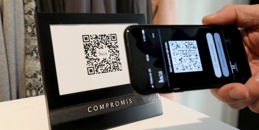 Eine Hand mit Handy vor einem Bildschirm mit QR-Code.