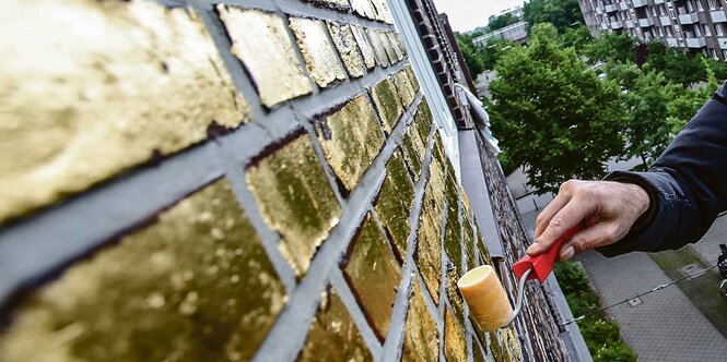 Eine Hand streicht eine Fassade gold.