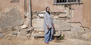 Eine Frau steht vor einer brüchigen Häuserwand