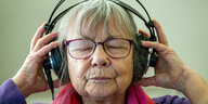 Eine ältere Frau trägt Kopfhörer und hat die Augen geschlossen