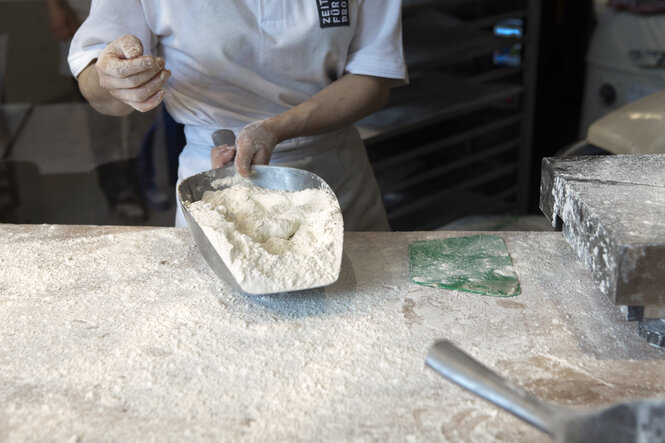 In der Backstube der Bäckerei "Zeit für Brot" Filiale im Prenzlauer Berg sieht man einen Bäcker mit einer Schaufel mit Mehl hantieren