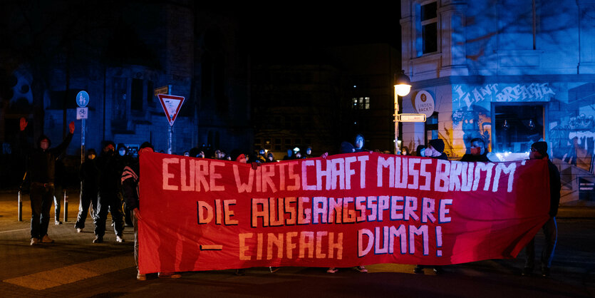 Linke Demonstranten mit einem Transparent "eure Wirtschaft muss brumm' - Ausgangssperre einfach dumm"