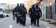 Fünf schwarz Uniformierte und maskierte Menschen im Gänsemarsch