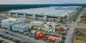 Eine riesige Halle der Tesla-Fabrik in Grünheide, im Vordergrund Baufahrzeuge