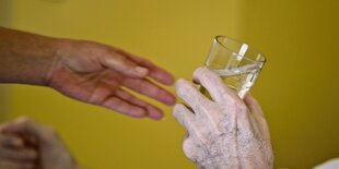 Die Hand einer jungen Person reicht der Hand einer alten Person ein Glas Wasser.