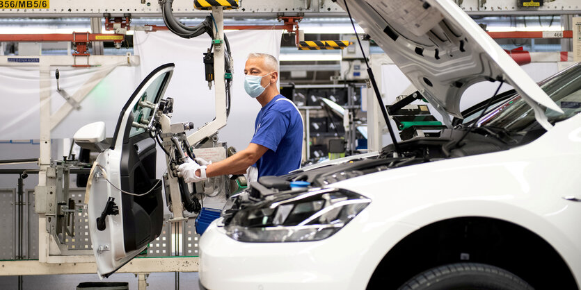 Ein VW Mitarbeiter arbeitet mit Mundschutz in der Fertigungsstrasse an einer Autotür