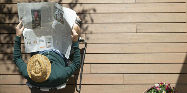 Ein Mann mit Sonnenhut liest auf seiner Terasse eine tageszeitung