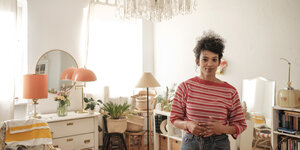 Autorin Elisa Aseva steht in ihrem hellen Wohnzimmer - an der Decke ein Kronleuchter