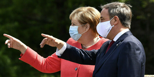 Angela Merkel und Armin Laschet mit Gesichtsmasken zeigen in die gleiche Richtung