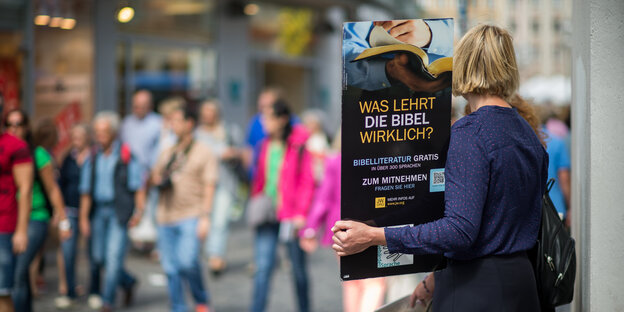 Eine Frau hält ein Schild mit der Aufschrift "Was lehrt die Bibel wirklich?" hoch