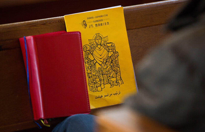 Ein rotes Buch und ein dünnes gelbes mit arabischen Schriftzeichen liegen auf einer Kirchenbank