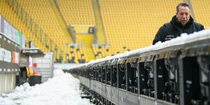 Leeres und verschneites Stadion. Ein Mann geht hinter einer Werbebande
