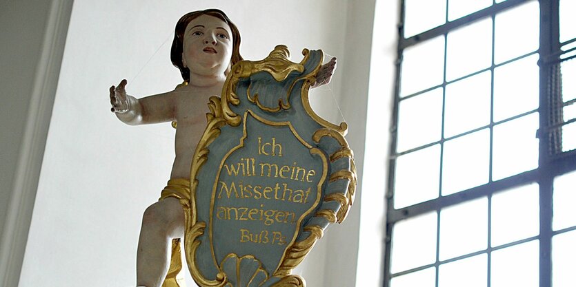 Eine Engelsfigur über einem Beichtstuhl hält eine Tafel mit dem Buß-Psalm "Ich will meine Missethat anzeigen"