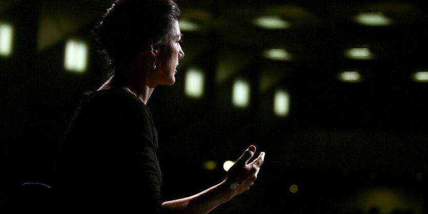 Sahra Wagenknecht sitzt auf einer Bühne im Dämmerlicht während einer Lesung