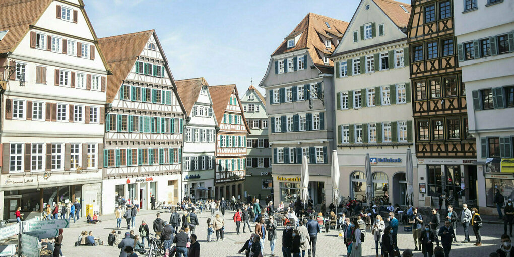 Menschen tummeln sich auf dem Tübinger Rathausplatz, im Hintergrund stehen alte Fachwerkhäuser